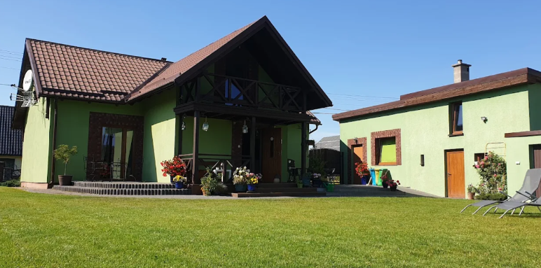 Zielony dom z drewnianym gankiem i ceglanymi wykończeniami, przed nim trawnik i leżaki